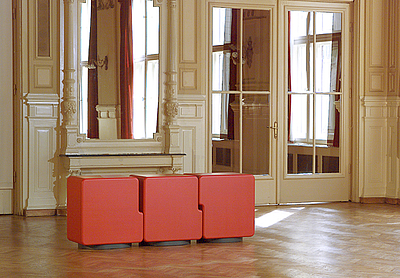 Orange-rotes Sideboard auf Holzboden, dahinter befindet sich ein großer Wandspiegel