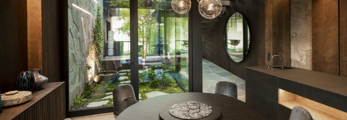 Innenaufnahme einer dunkelbraunen Küche mit Tisch und Blick in einen begrünten Innenhof ©Andreas Balon